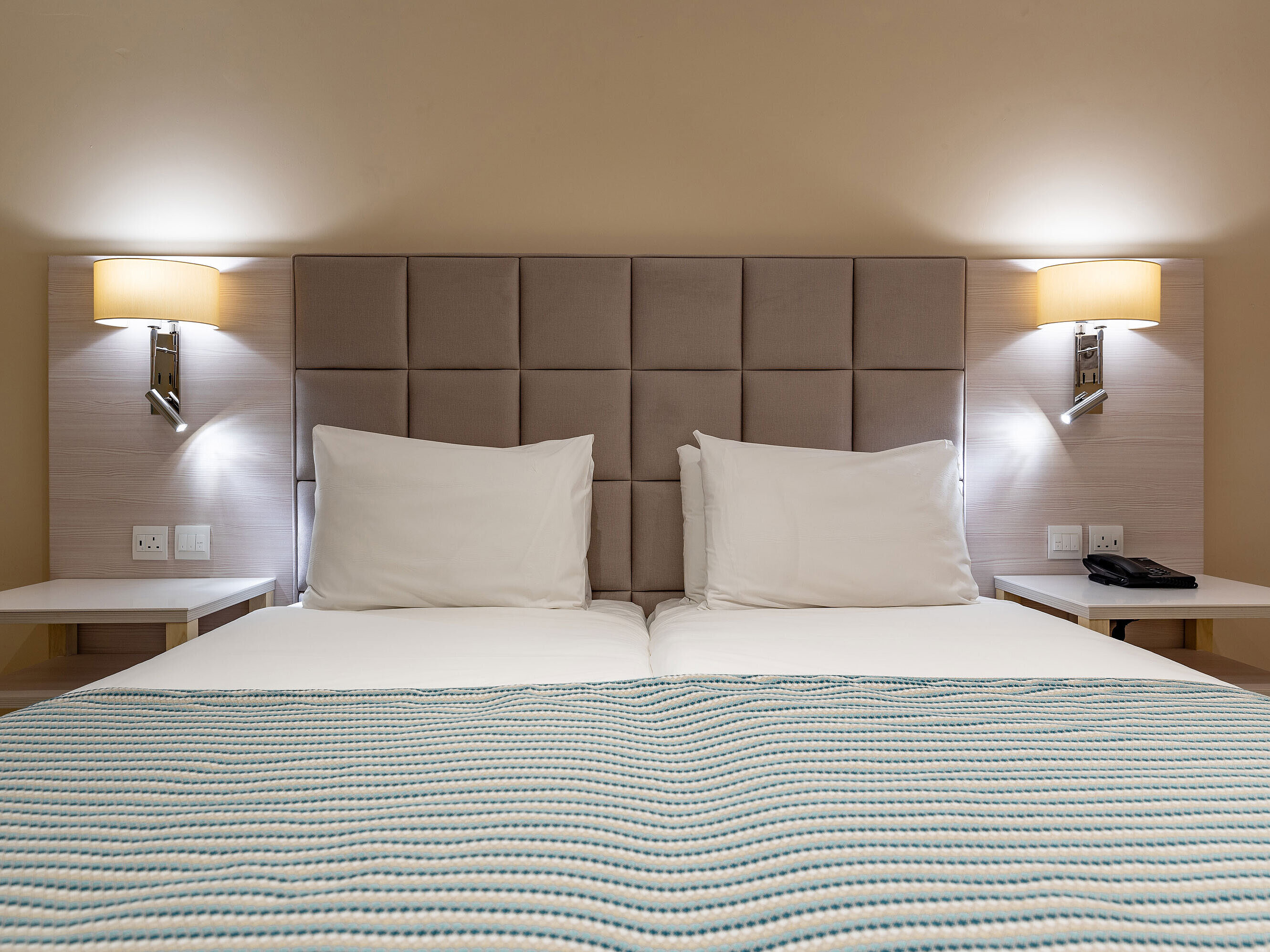 Classic double bed with padded headboard, bedside tables and reading lamps in a hotel room