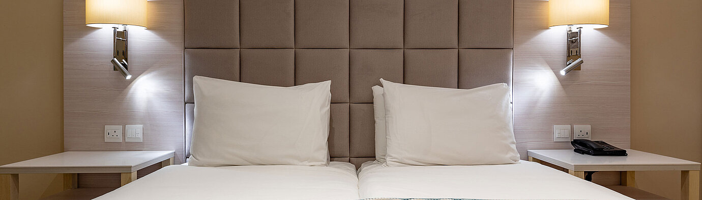 Classic double bed with padded headboard, bedside tables and reading lamps in a hotel room