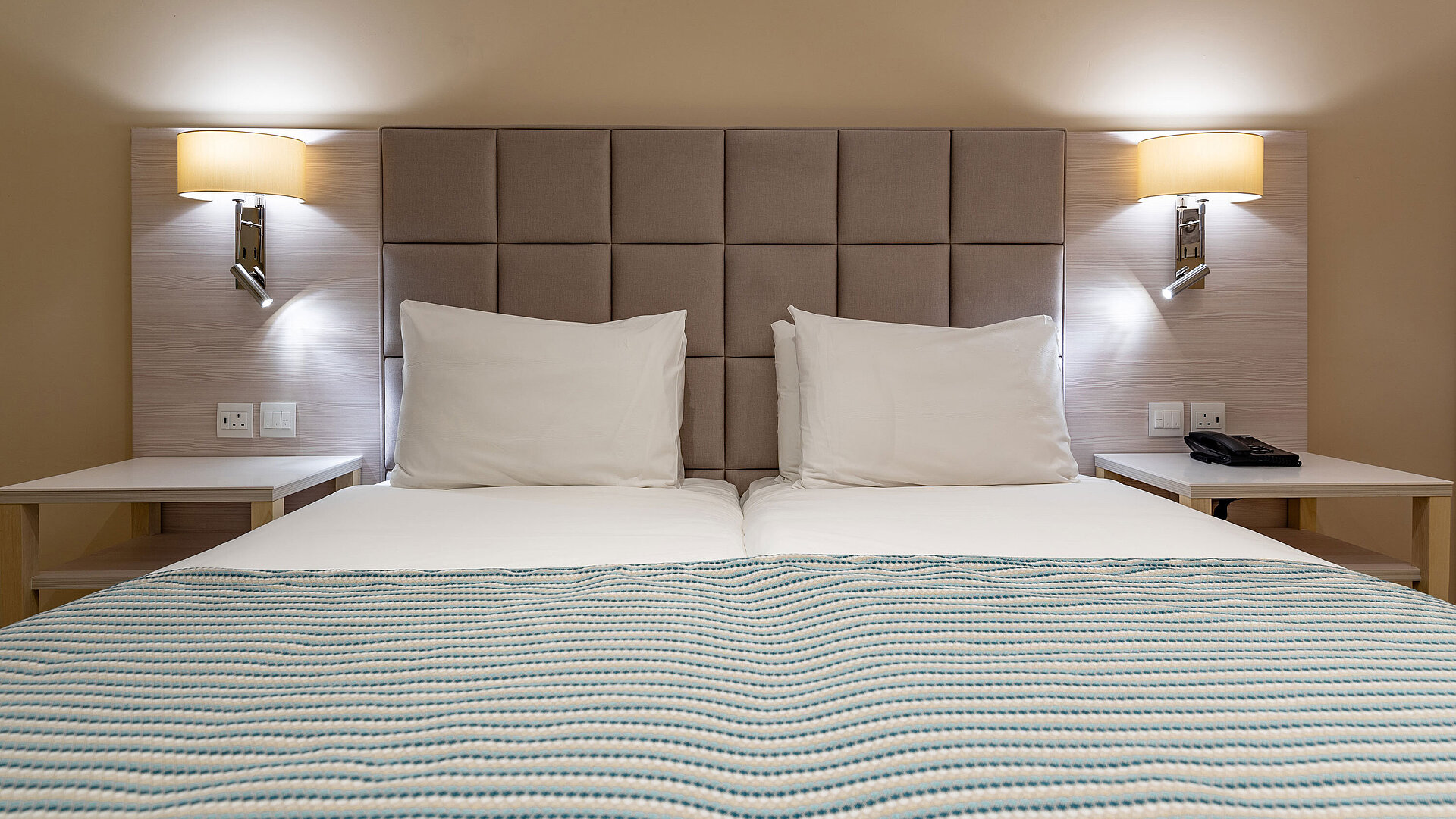 Classic double bed with padded headboard, bedside tables and reading lamps in a hotel room
