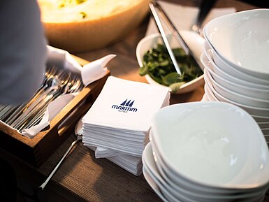 Stacked white bowls, Maritim-branded napkins and cutlery arranged on a buffet station.