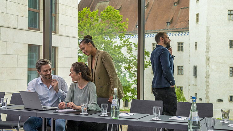 Smiling business people in the meeting room at Maritim Hotel Ingolstadt with a view of historic buildings.