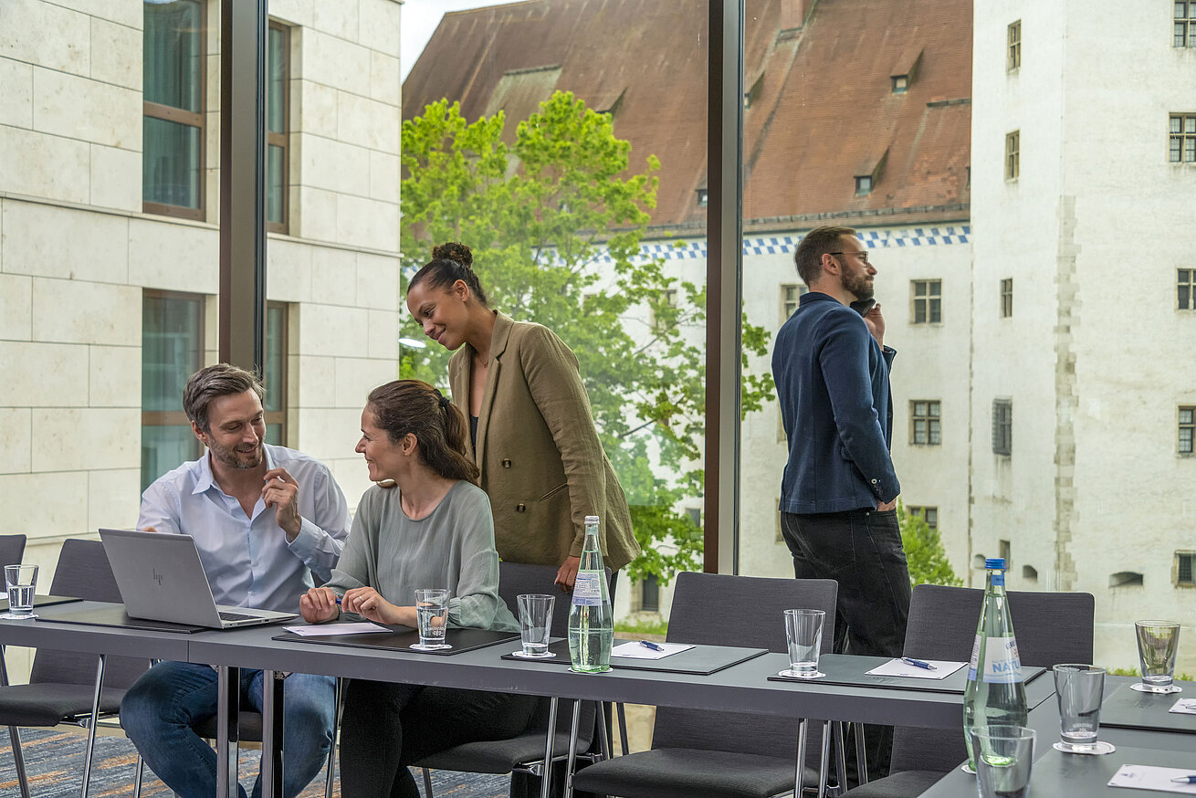 Smiling business people in the meeting room at Maritim Hotel Ingolstadt with a view of historic buildings.
