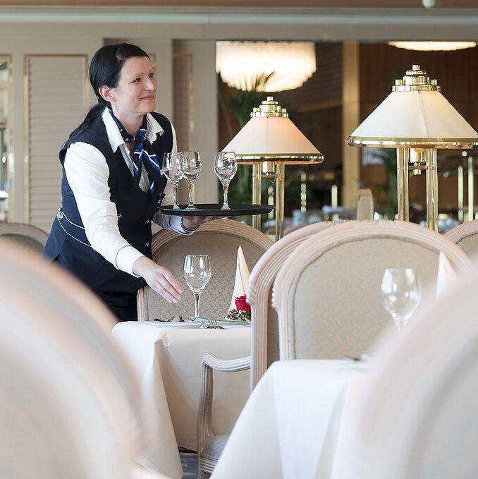 Waitress sets a table in the restaurant of the Maritim Hotel Timmendorfer Strand, with an elegant atmosphere and glass lamps.