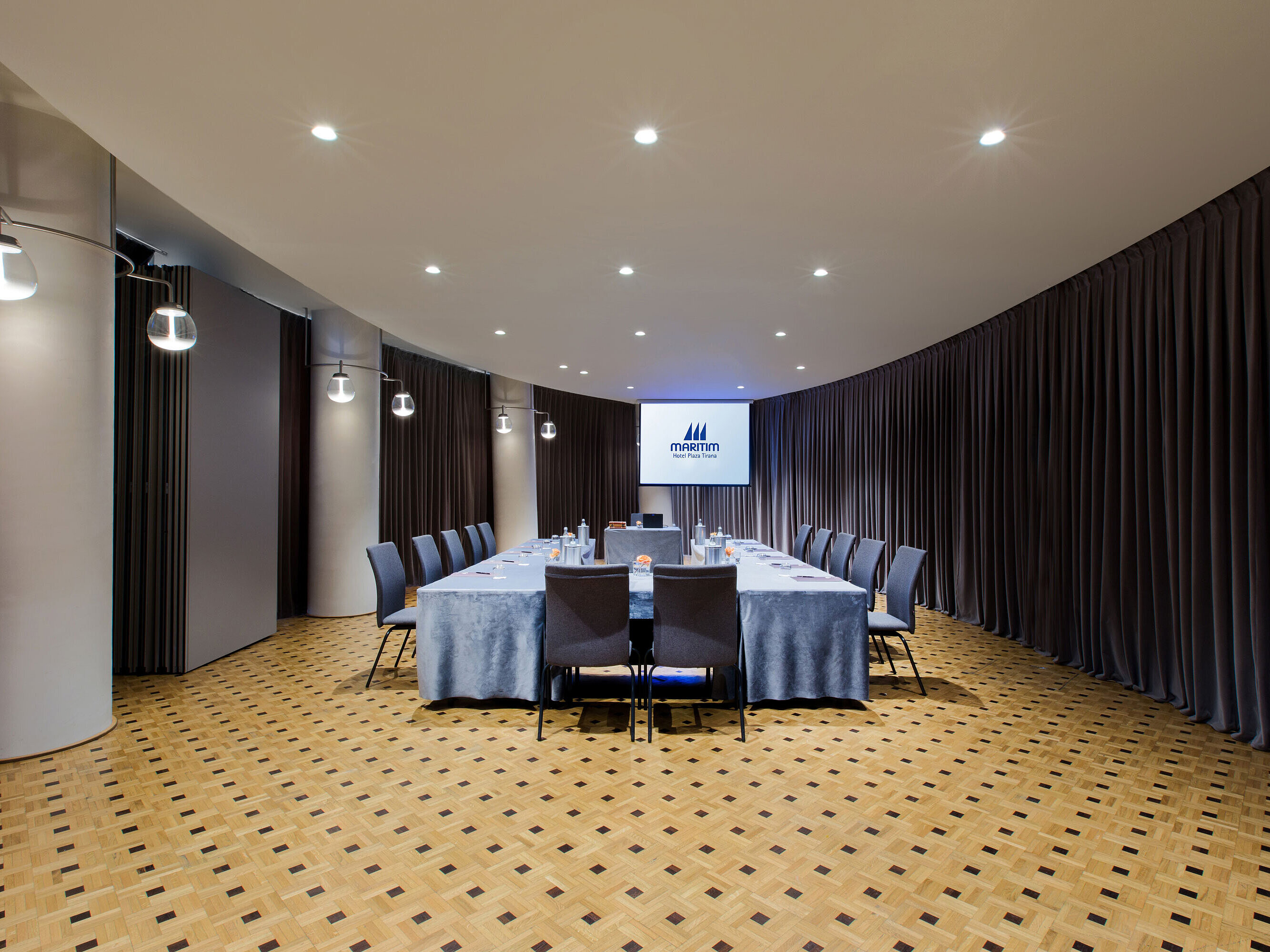 Modern meeting room at Maritim Hotel Plaza Tirana with U-shape seating, screen and elegant curtain design