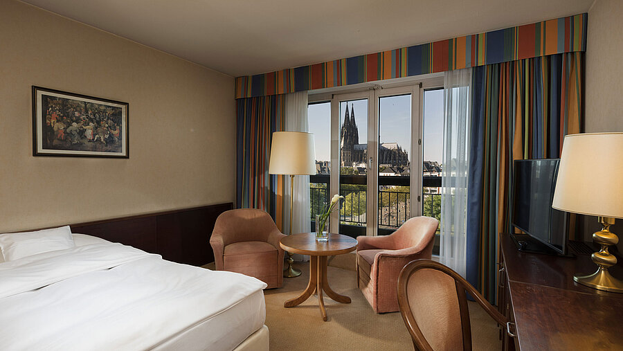 Superior room at Maritim Hotel Cologne featuring a seating area, comfortable bed, and view of Cologne Cathedral.