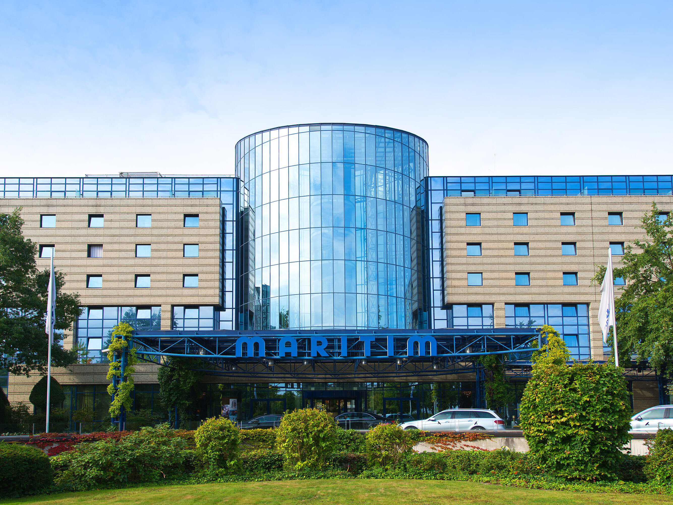 Exterior view of the Maritim Hotel Bonn with a modern glass facade and well-kept garden in the foreground.
