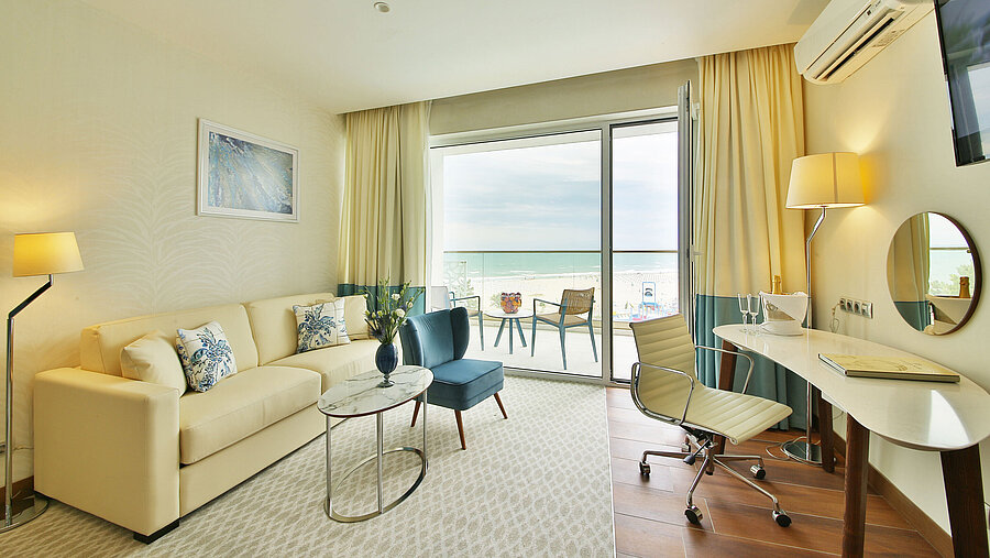 Bright hotel room with sofa, desk and balcony offering a sea view