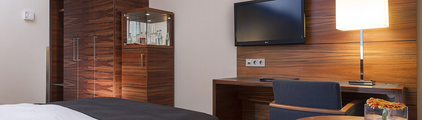 Modern room in the Maritim Hotel Munich with workspace, TV, seating area, and large wardrobe.