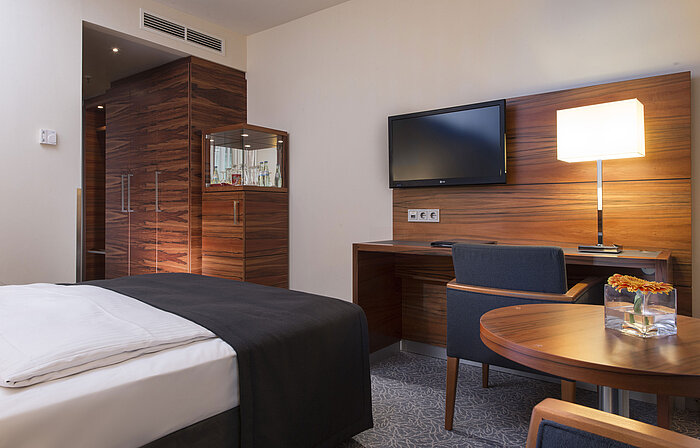 Modern room in the Maritim Hotel Munich with workspace, TV, seating area, and large wardrobe.