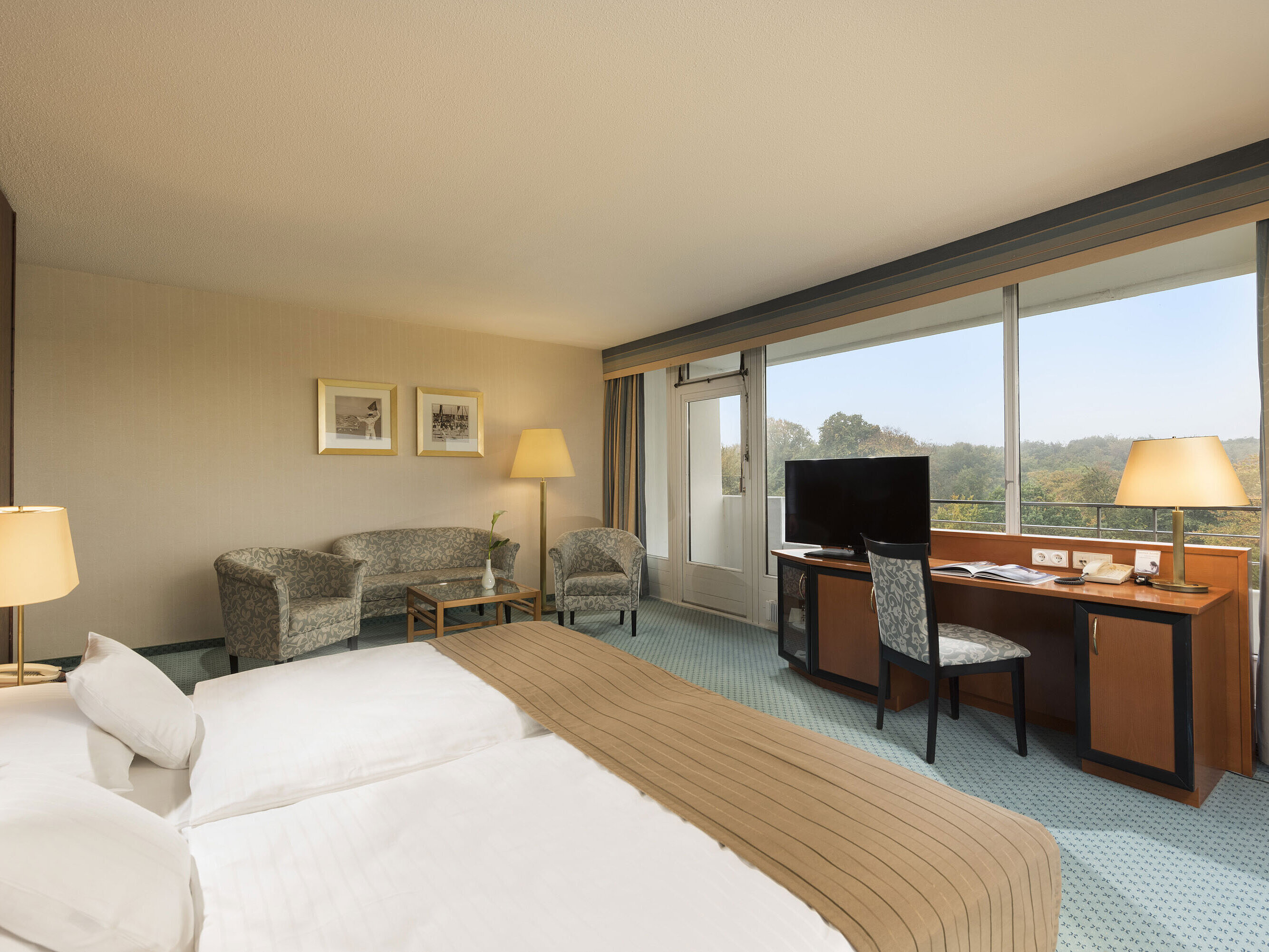 Comfort room at the Maritim Hotel Kiel with a cozy seating area, desk, large bed and a wonderful view of the countryside.