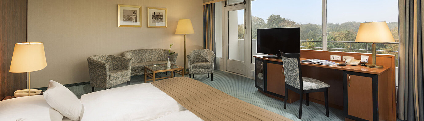 Comfort room at the Maritim Hotel Kiel with a cozy seating area, desk, large bed and a wonderful view of the countryside.