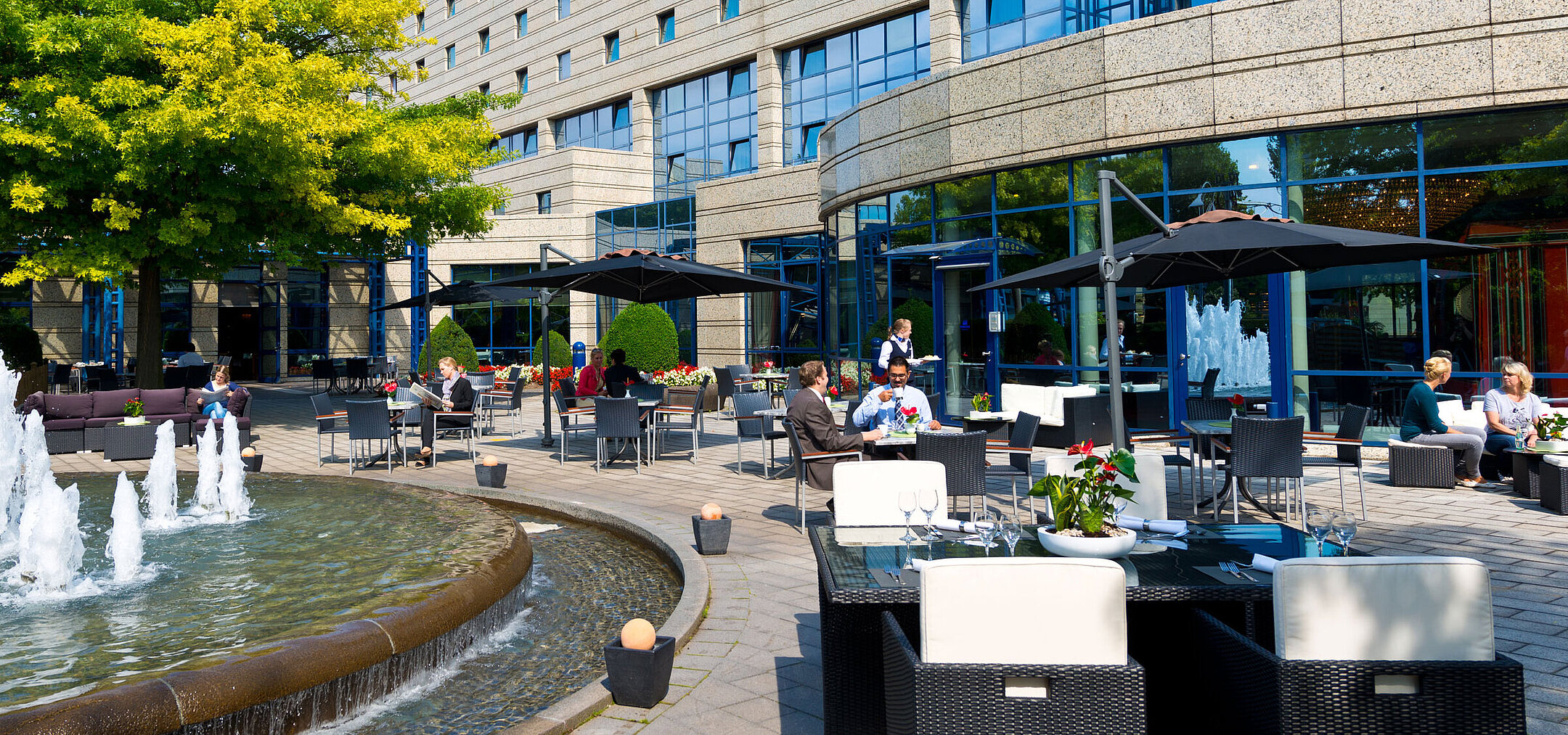 Terrace of the Maritim Hotel Bonn with seating areas, fountain, and guests dining and relaxing outdoors.