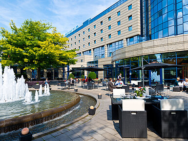 Terrace of the Maritim Hotel Bonn with seating areas, fountain, and guests dining and relaxing outdoors.