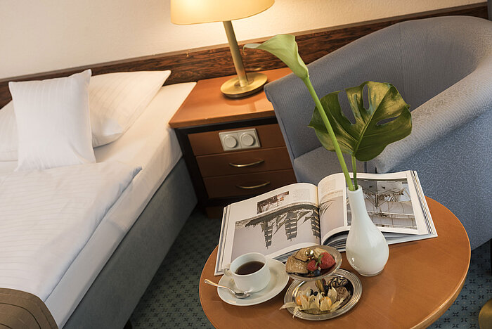 Details of a room at the Maritim Hotel Kiel: side table with vase, book and snacks next to a bed and armchair.
