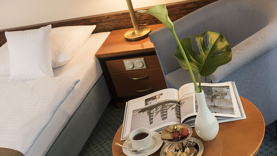 Details of a room at the Maritim Hotel Kiel: side table with vase, book and snacks next to a bed and armchair.