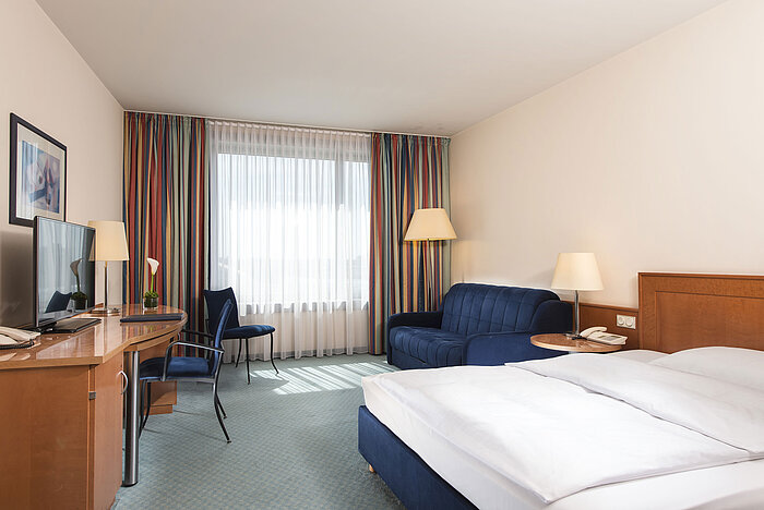 Classic room at Maritim Hotel Frankfurt with double bed, desk, sofa, and large windows for natural light.