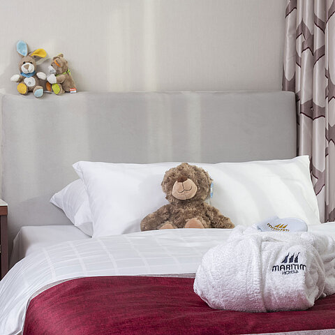 Family suite at the Maritim Hotel Bonn featuring a cozy bed, stuffed toys, and a bathrobe, perfect for kids.