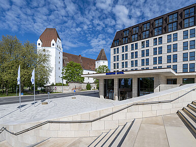 The modern Maritim Hotel Ingolstadt with the historic Neues Schloss in the background and a welcoming entrance.