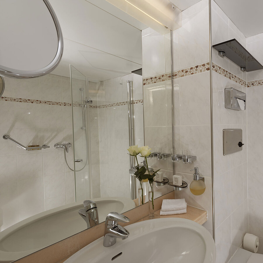 Bright bathroom at Maritim Hotel Bad Salzuflen with shower, large mirror and white tiles