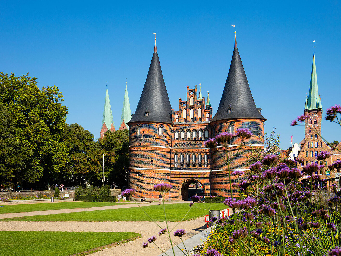 Holstentor in Lübeck with blooming flowers in the foreground and blue sky.
