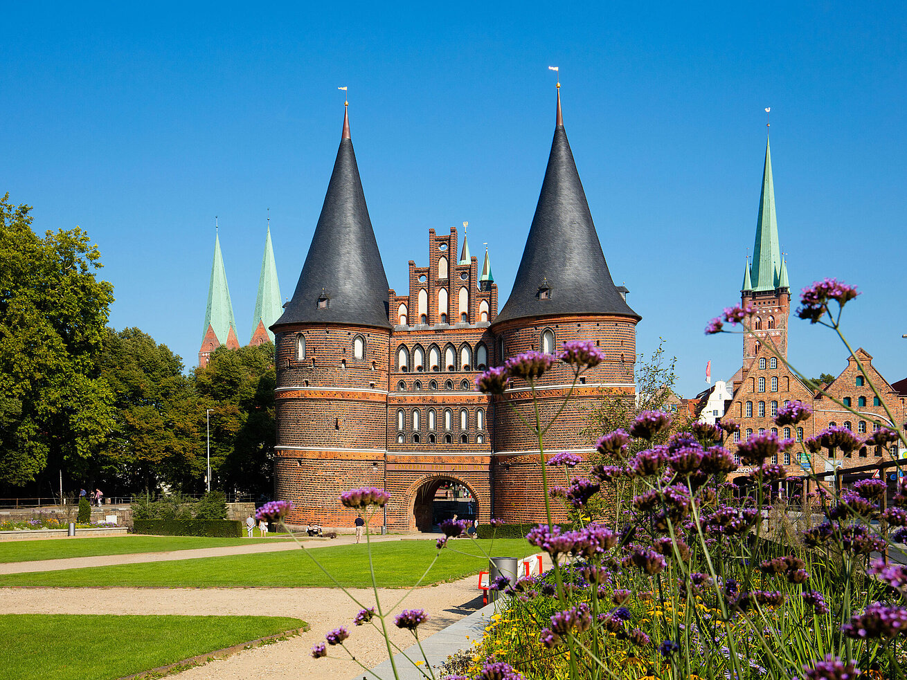 Holstentor in Lübeck with blooming flowers in the foreground and blue sky.