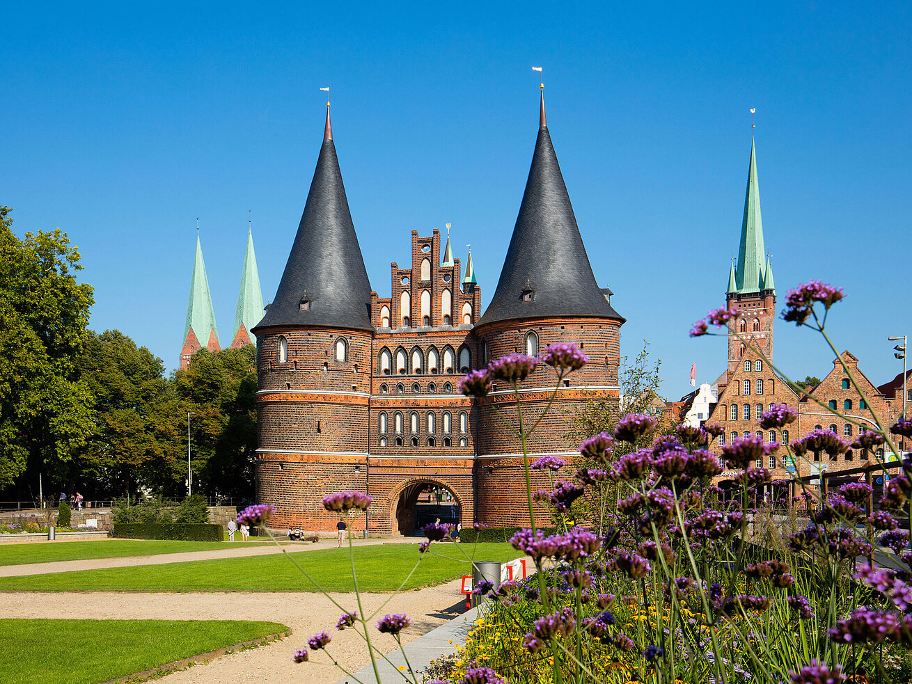 Holstentor in Lübeck with blooming flowers in the foreground and blue sky.