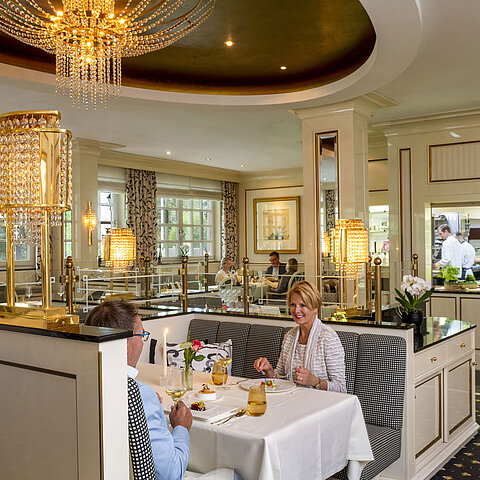 Couple enjoying a fine dinner at the luxurious Orangerie restaurant in Maritim Timmendorfer Strand with a view of the kitchen