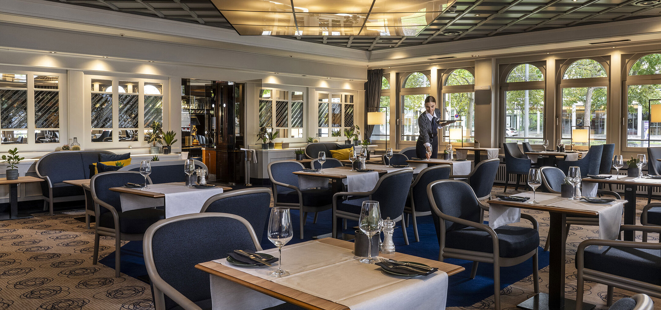 Modern restaurant at Maritim Hotel Darmstadt with set tables and elegant design. A staff member is providing service.
