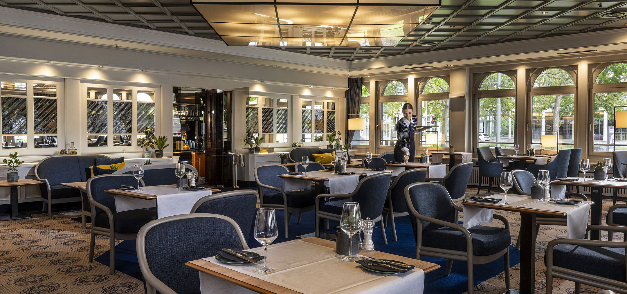 Modern restaurant at Maritim Hotel Darmstadt with set tables and elegant design. A staff member is providing service.