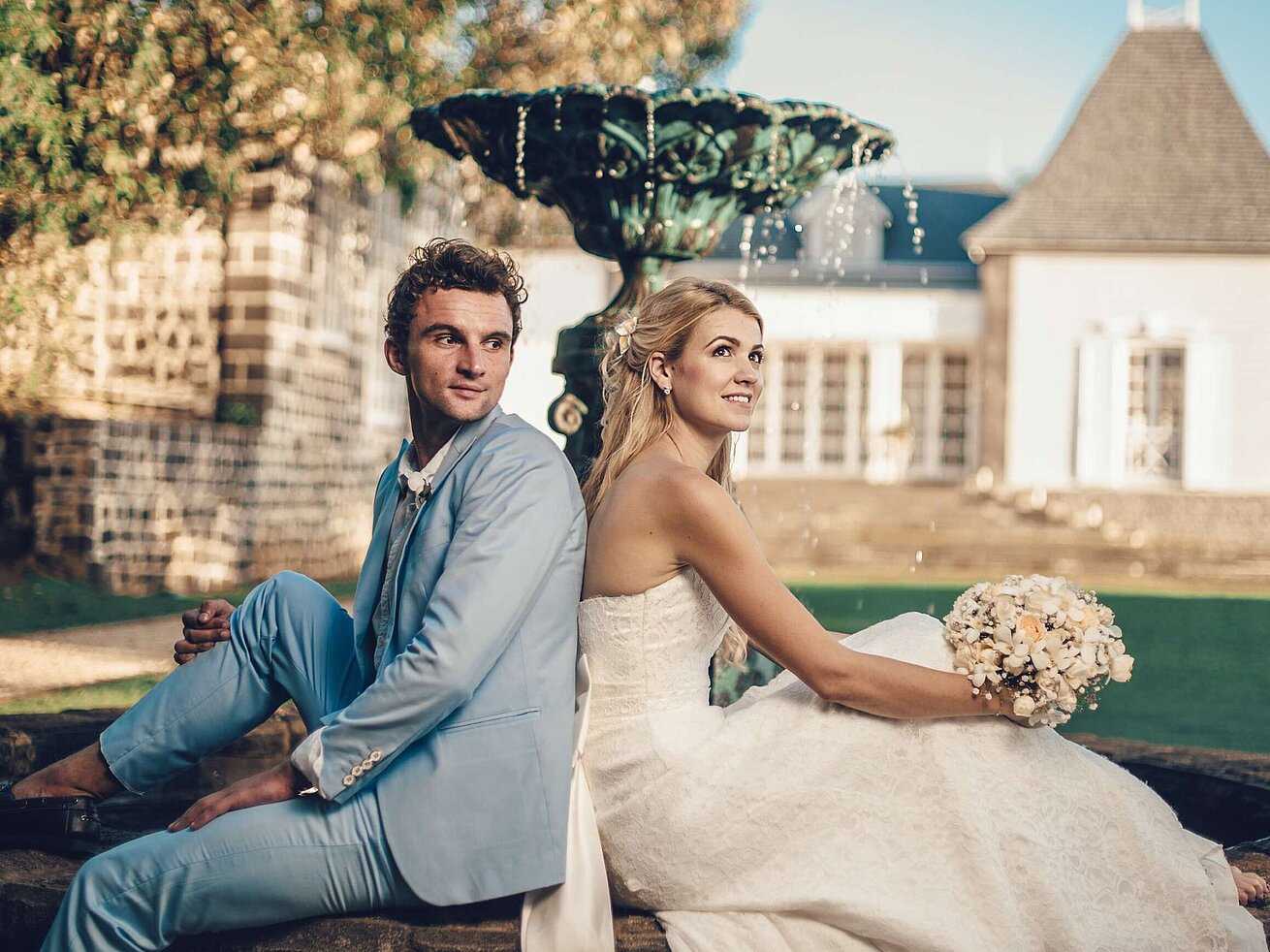 Wedding couple sitting back to back by a fountain enjoying romantic moments in the garden