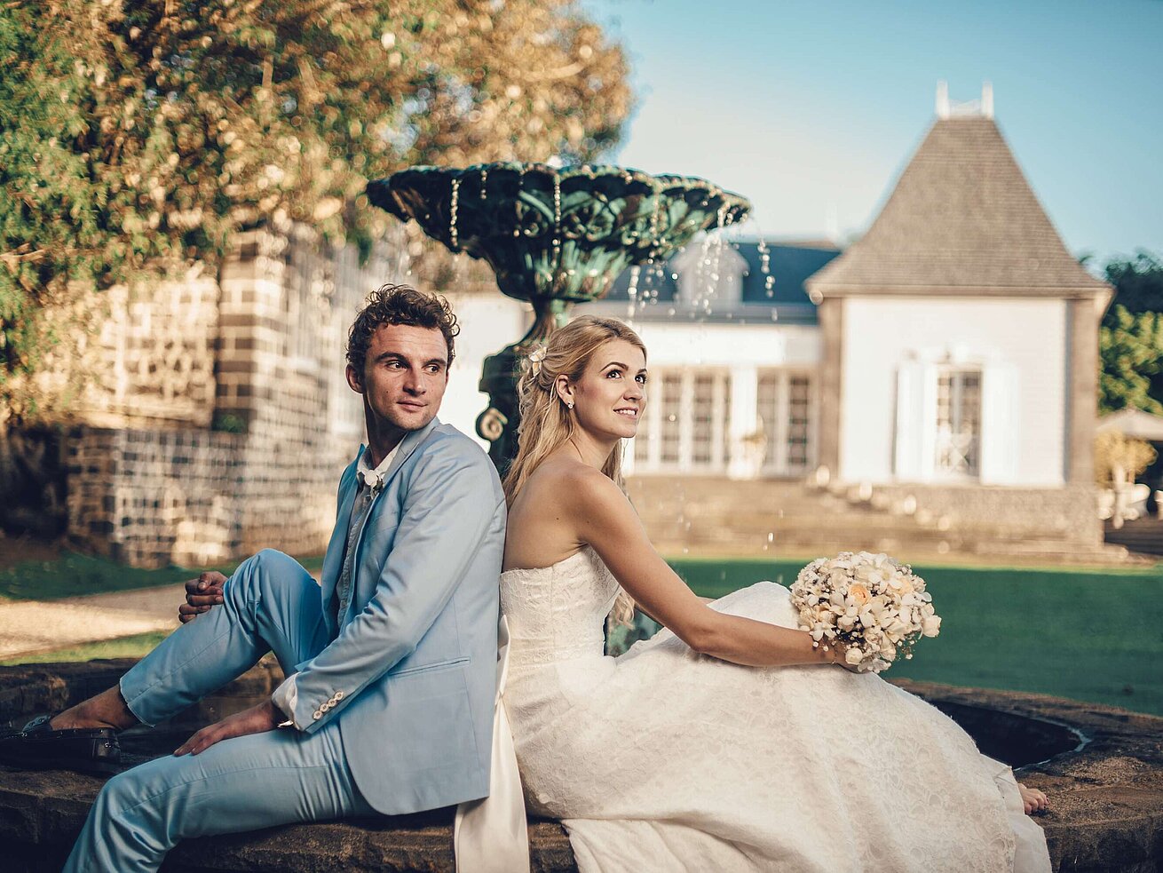 Wedding couple sitting back to back by a fountain enjoying romantic moments in the garden