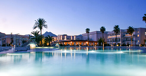 Evening lights at the pool of Maritim Resort Calabria with palm trees and mountain backdrop