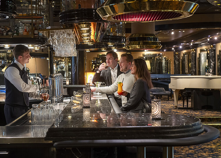 Guests enjoy cocktails at the piano bar in the Maritim Hotel Cologne, while the bartender serves them.