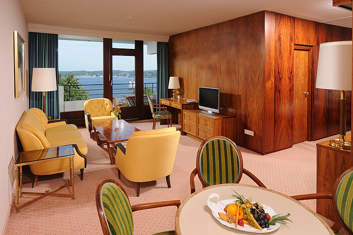Junior Suite in the Maritim Hotel Kiel, cozy sitting area, desk, TV and balcony with a view of the water.