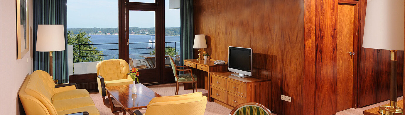Junior suite Junior Suite in the Maritim Hotel Kiel, cozy sitting area, desk, TV and balcony with a view of the water.
