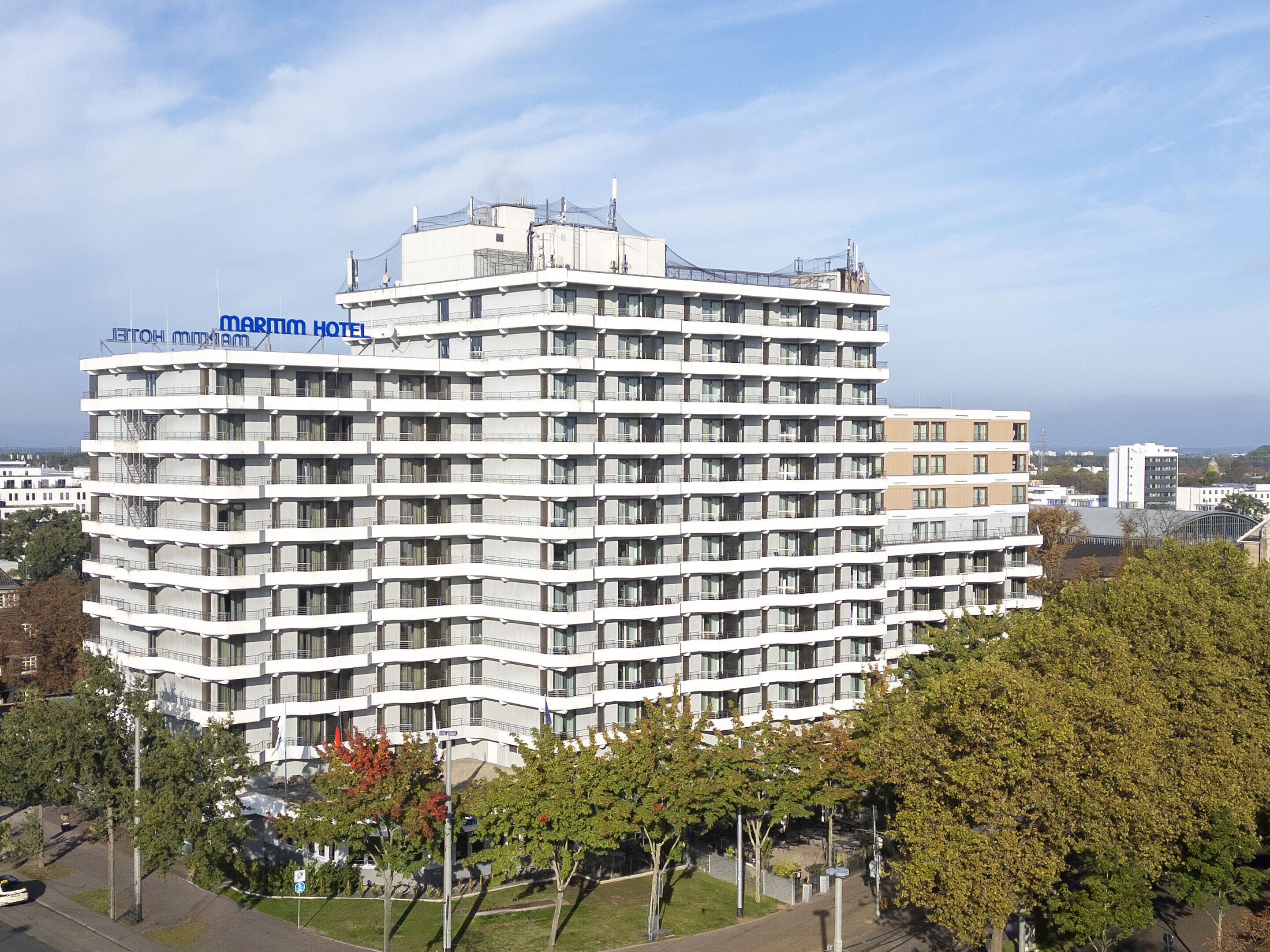 Exterior view of the Maritim Hotel Darmstadt with modern architecture and green trees in the foreground.
