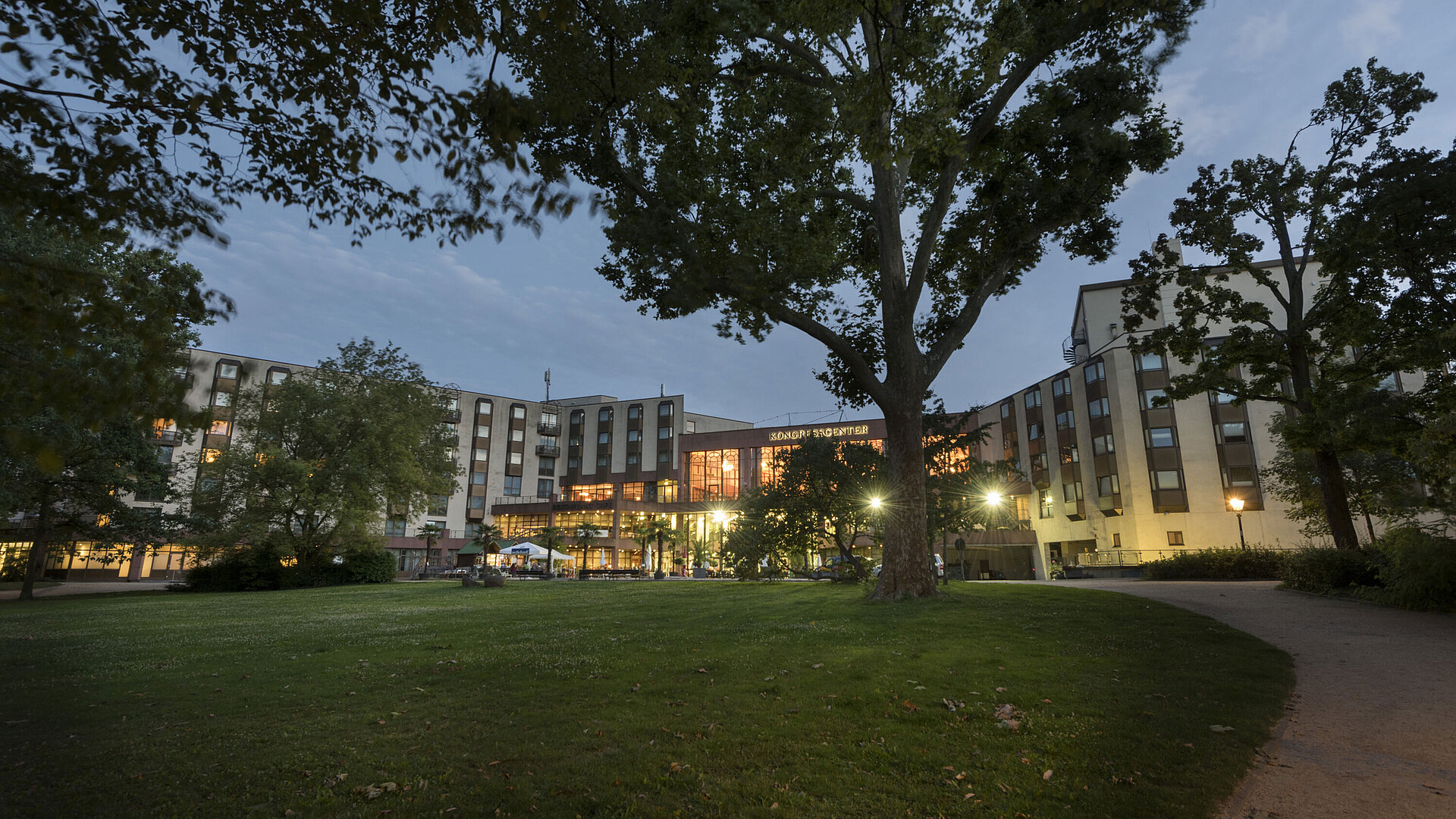View of Maritim Hotel Bad Homburg from the green park at dusk, illuminated congress center.
