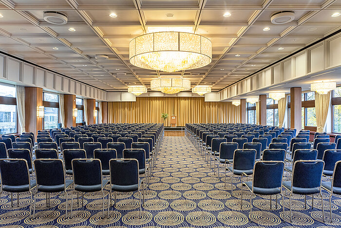 Saal Maritim in the Maritim Hotel Kiel, large conference room with row seating, chandeliers and a stage in front of a curtain.
