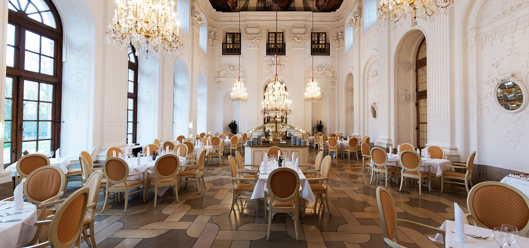 Elegant Apollo Hall at Maritim Hotel Fulda with chandeliers, fresco ceiling, and stylishly set tables.
