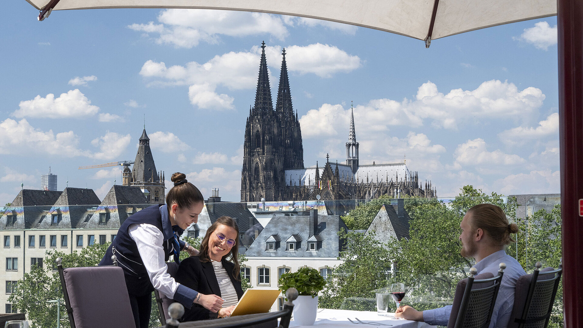 Guests enjoying service on the rooftop terrace of Maritim Hotel Cologne with views of Cologne Cathedral and the Old Town.