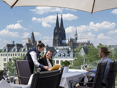 Guests enjoying service on the rooftop terrace of Maritim Hotel Cologne with views of Cologne Cathedral and the Old Town.