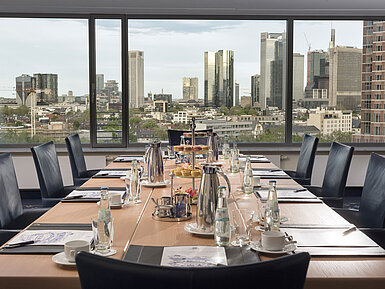 Conference room at Maritim Hotel Frankfurt with a skyline view. Elegant table set with beverages and snacks for meetings.