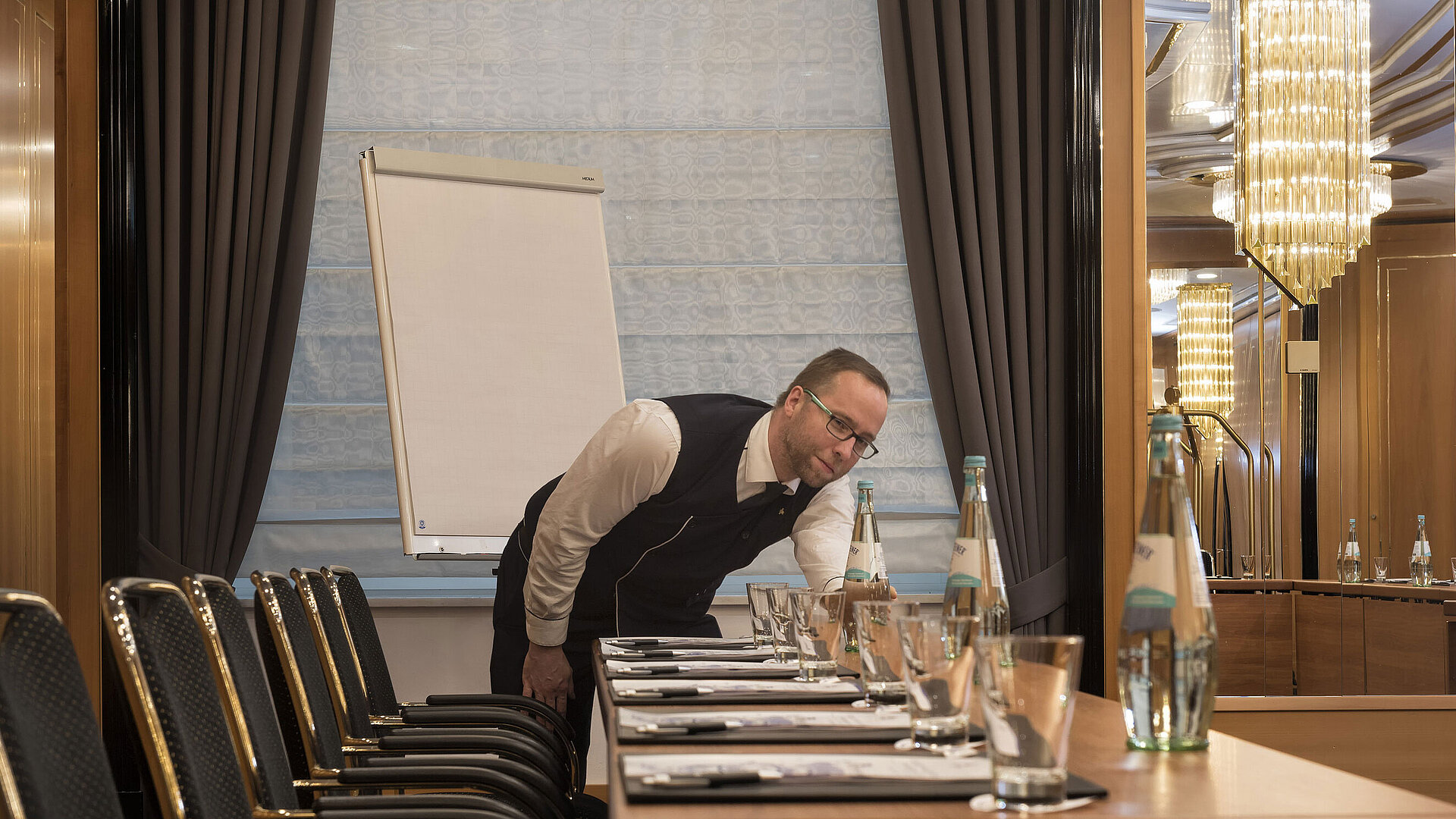 Staff member prepares conference table with water bottles and glasses at Maritim Hotel Stuttgart
