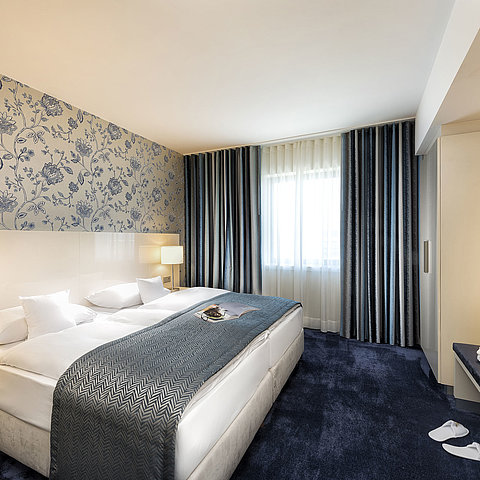 Elegant suite at Maritim Hotel Bonn with a large bed, blue bedspread, and stylish decor.