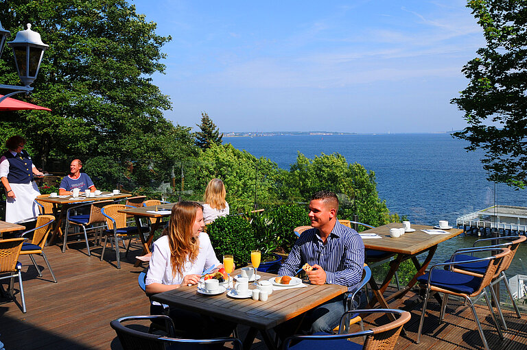 Panorama terrace at the Maritim Hotel Kiel with guests enjoying breakfast, a view of the fjord, sunny weather and a relaxed atmosphere.