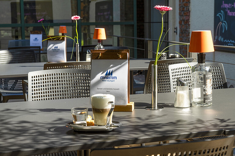 Cappuccino, water and pastry on the sunny terrace of the Maritim Hotel Stuttgart with a menu