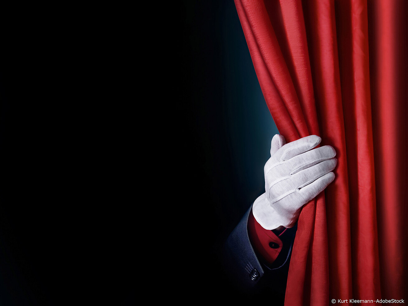 White gloved hand pulling open red theatre curtain