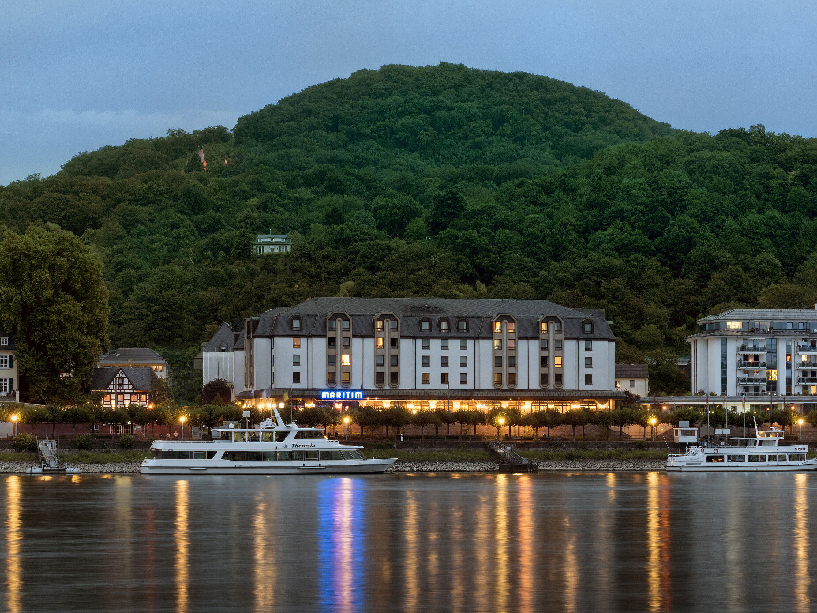 Maritim Hotel Königswinter at night with atmospheric lighting and a view of the Rhine.