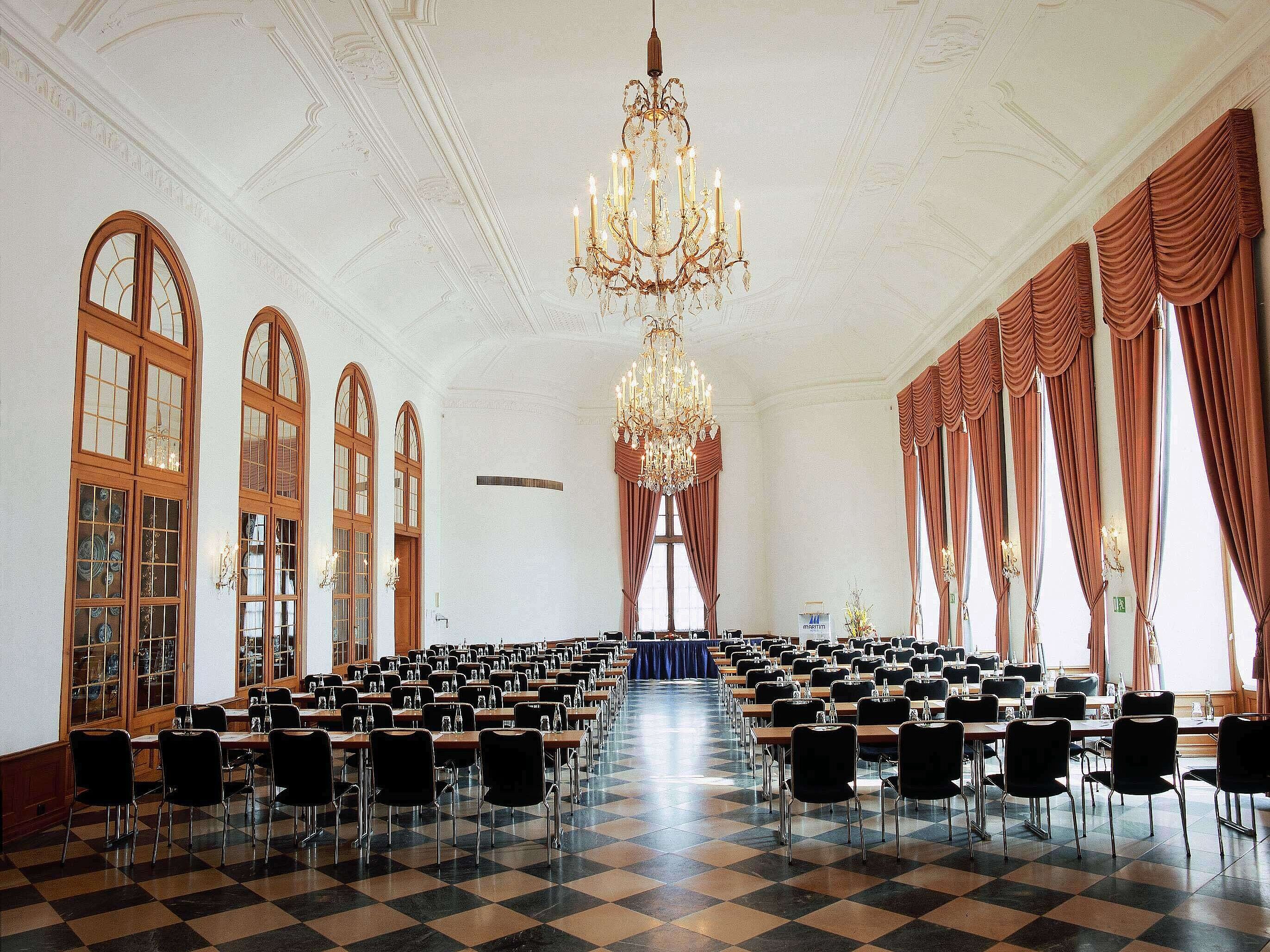 Elegant event hall at Maritim Hotel Fulda with chandeliers, high windows, and stylish seating for events.