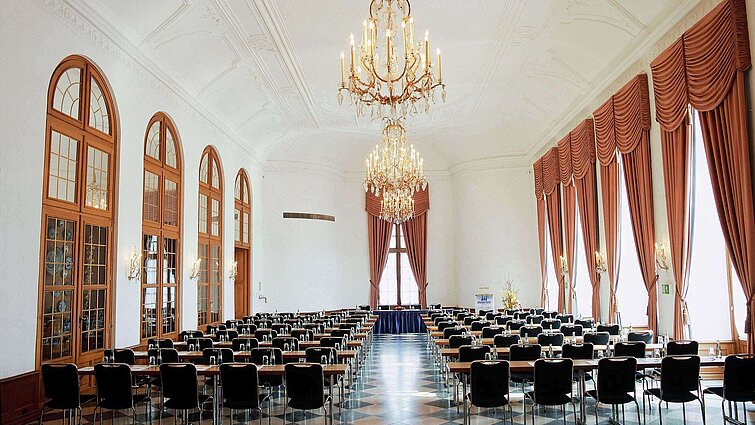 Elegant event hall at Maritim Hotel Fulda with chandeliers, high windows, and stylish seating for events.